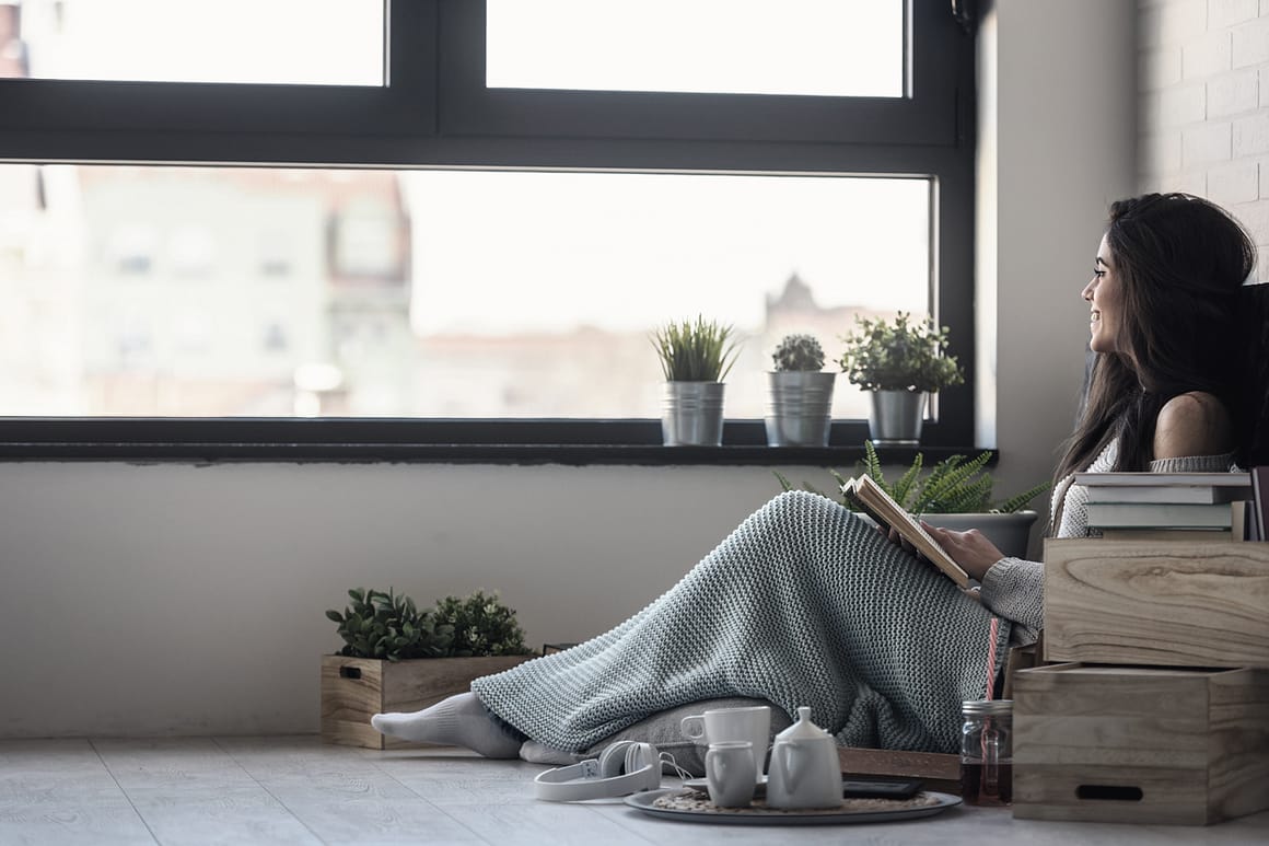 Authentisch wohnen Frau sitzt auf dem Boden und schaut durch das Fenster